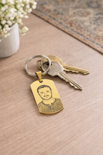Personalisierter goldfarbener Edelstahl-Anhänger mit individueller Foto-Gravur als Schlüsselanhänger, befestigt an einem Schlüsselring mit mehreren Schlüsseln. Dekorativ auf einem Holztisch arrangiert, hochwertig und alltagstauglich.